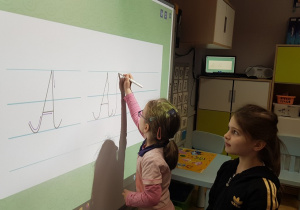 Dziewczynka ćwiczy pisanie litery na tablicy interaktywnej